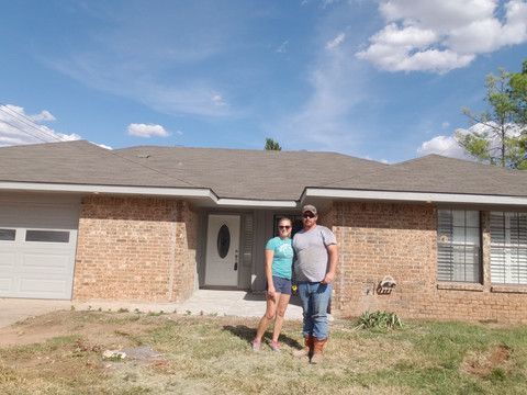 A man and a woman are standing in front of a brick house.