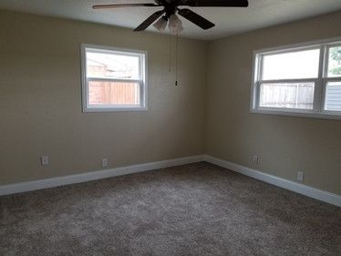 An empty bedroom with a ceiling fan and two windows.