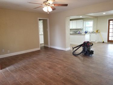 An empty living room with a vacuum cleaner on the floor and a ceiling fan.