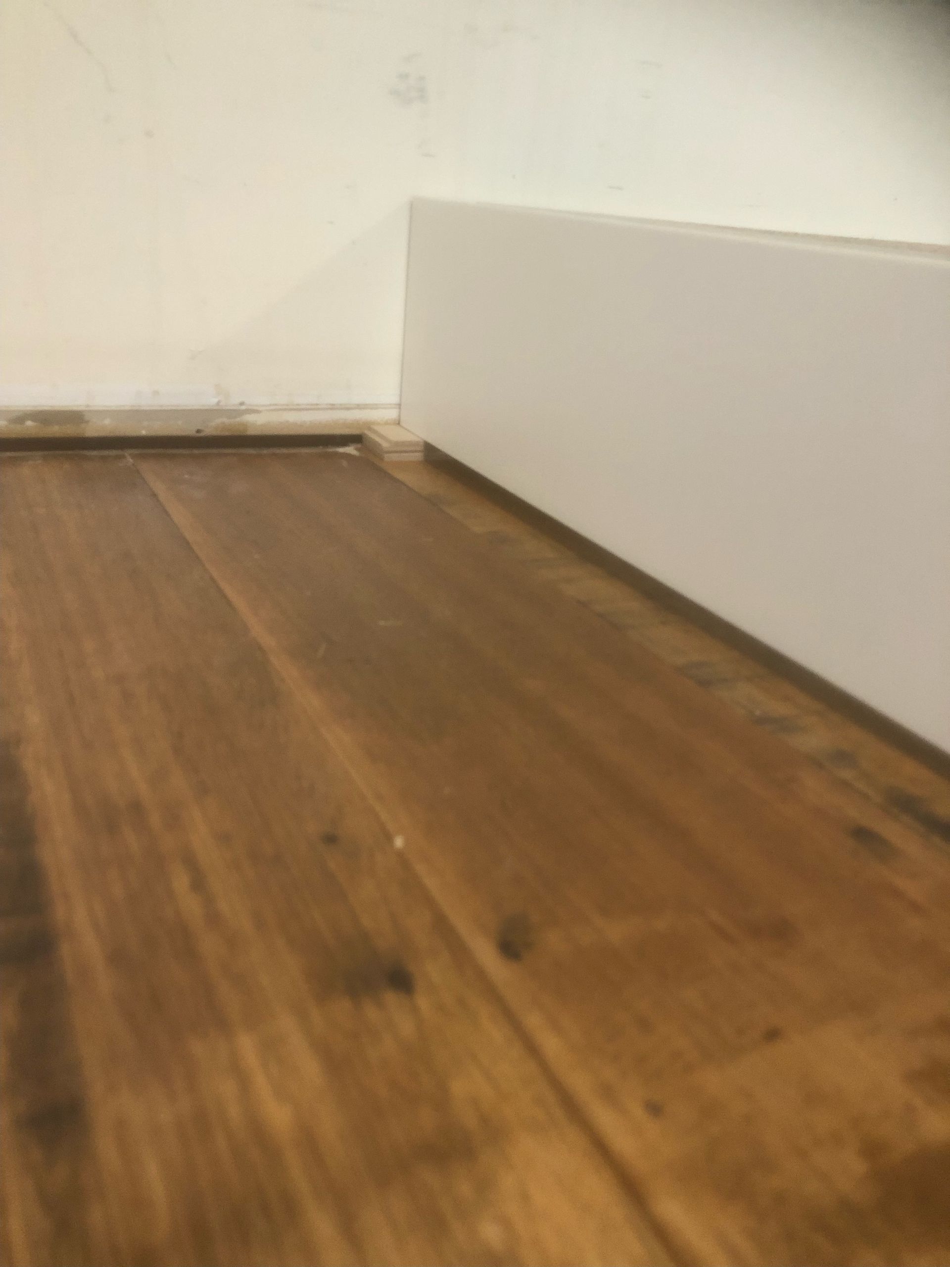 Wooden floor next to white baseboard and wall.