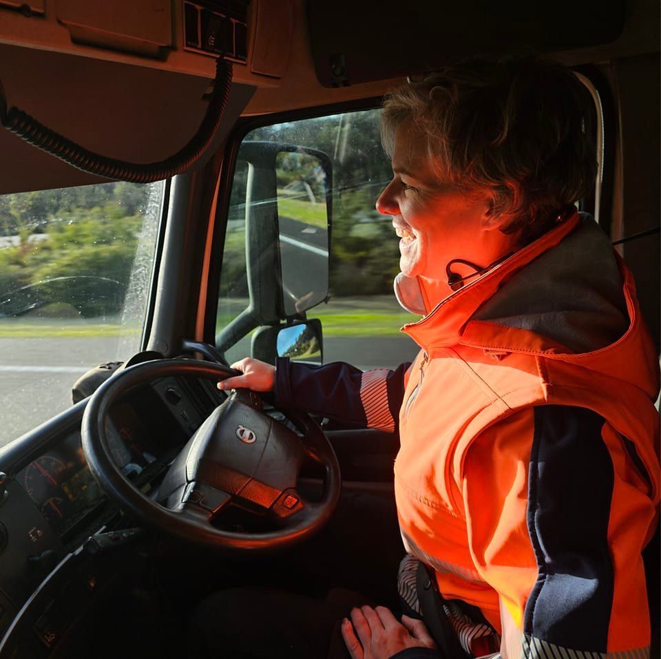 A woman in an orange vest is driving a truck