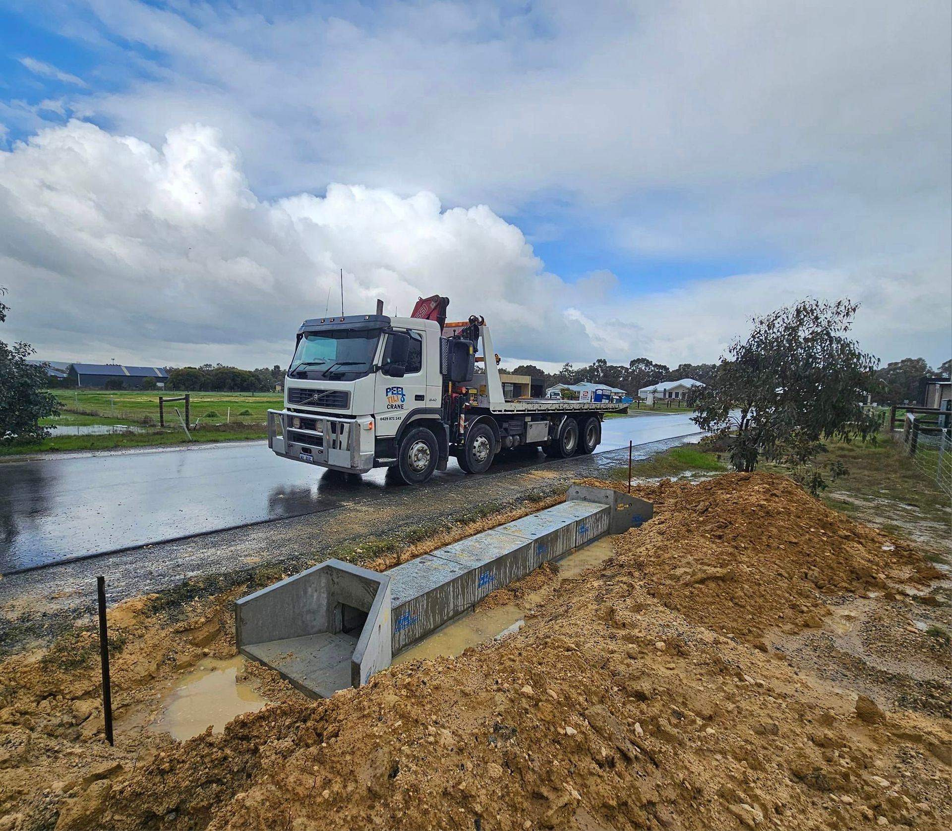 A white truck is driving down a road next to a pile of dirt.