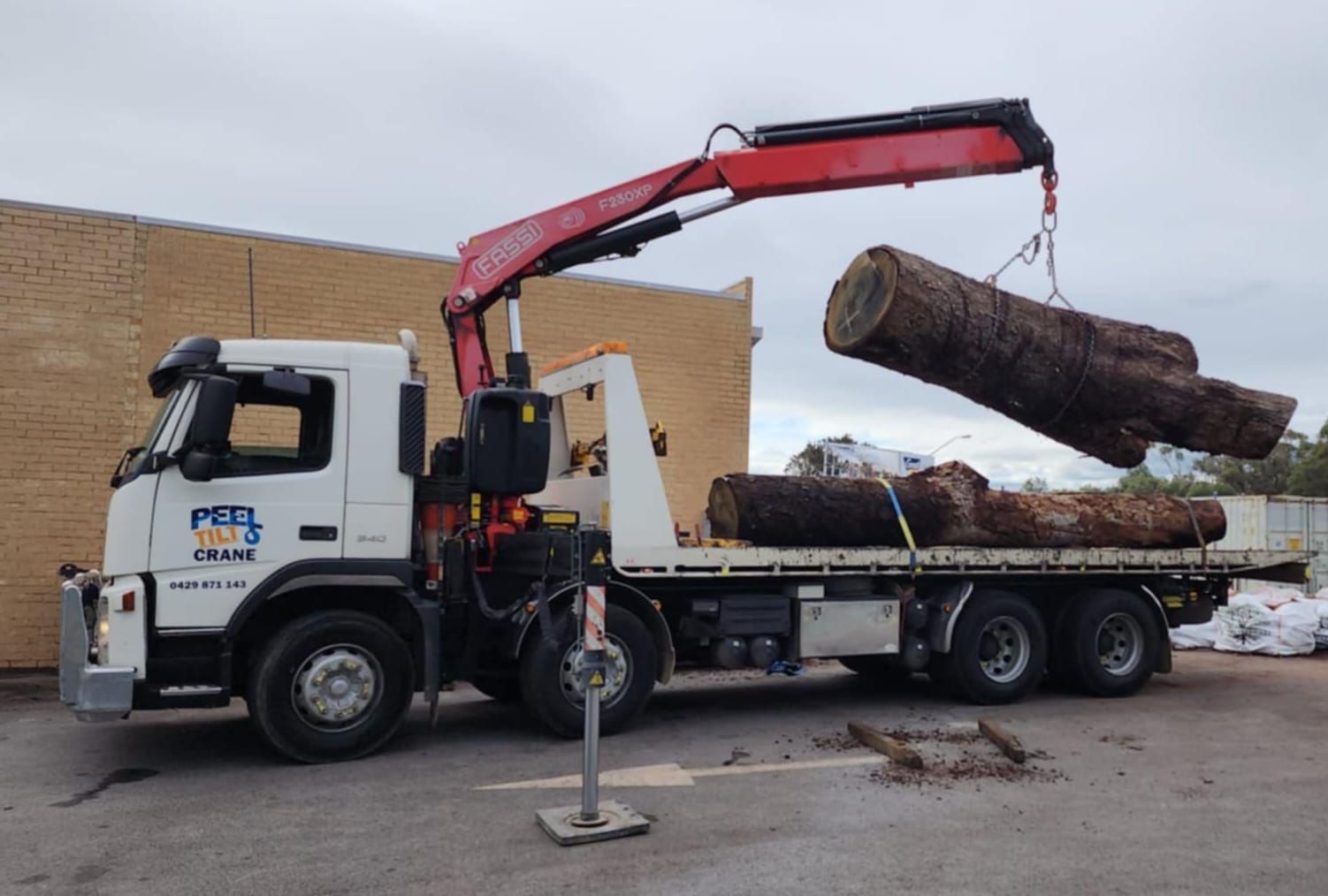A large log is being lifted by a crane on a flatbed truck.