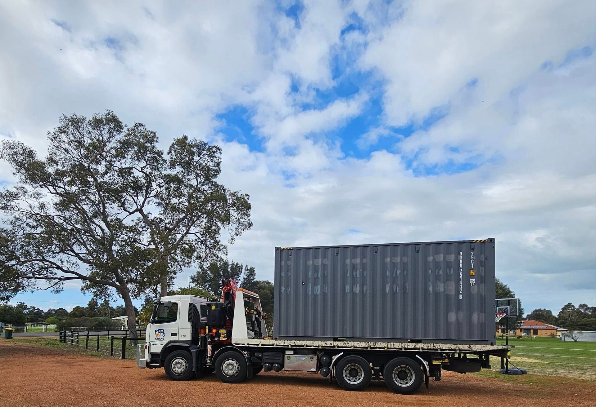 A truck with a container on the back is parked in a dirt field.