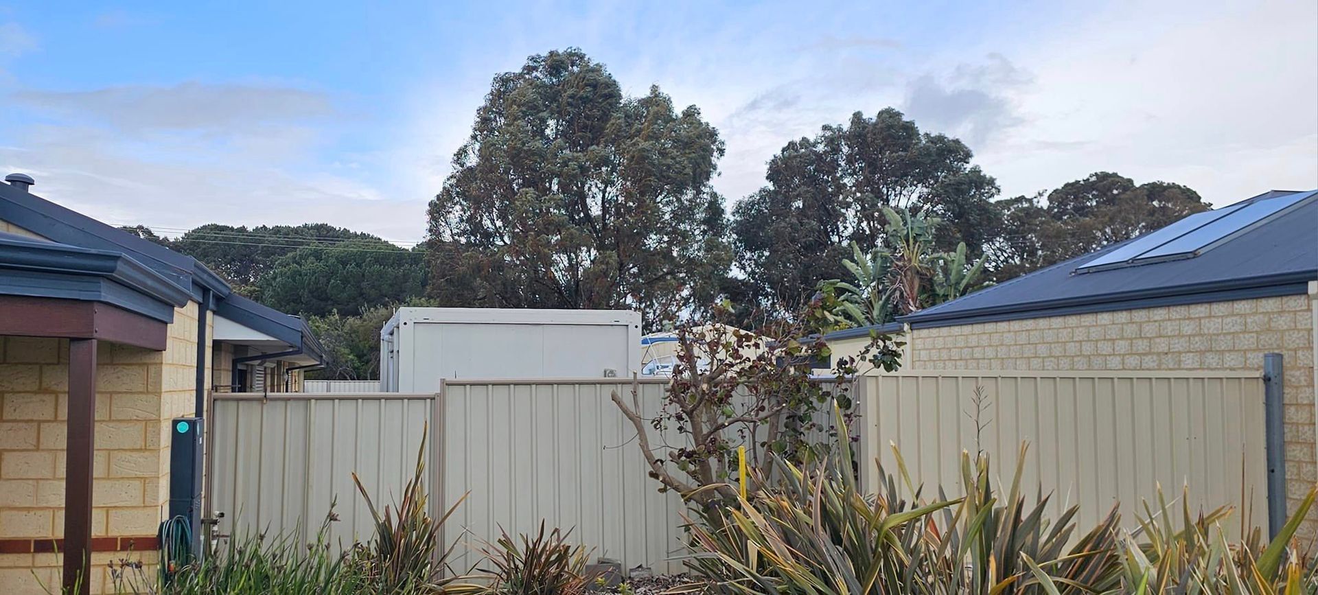 There is a fence between two houses with trees in the background.