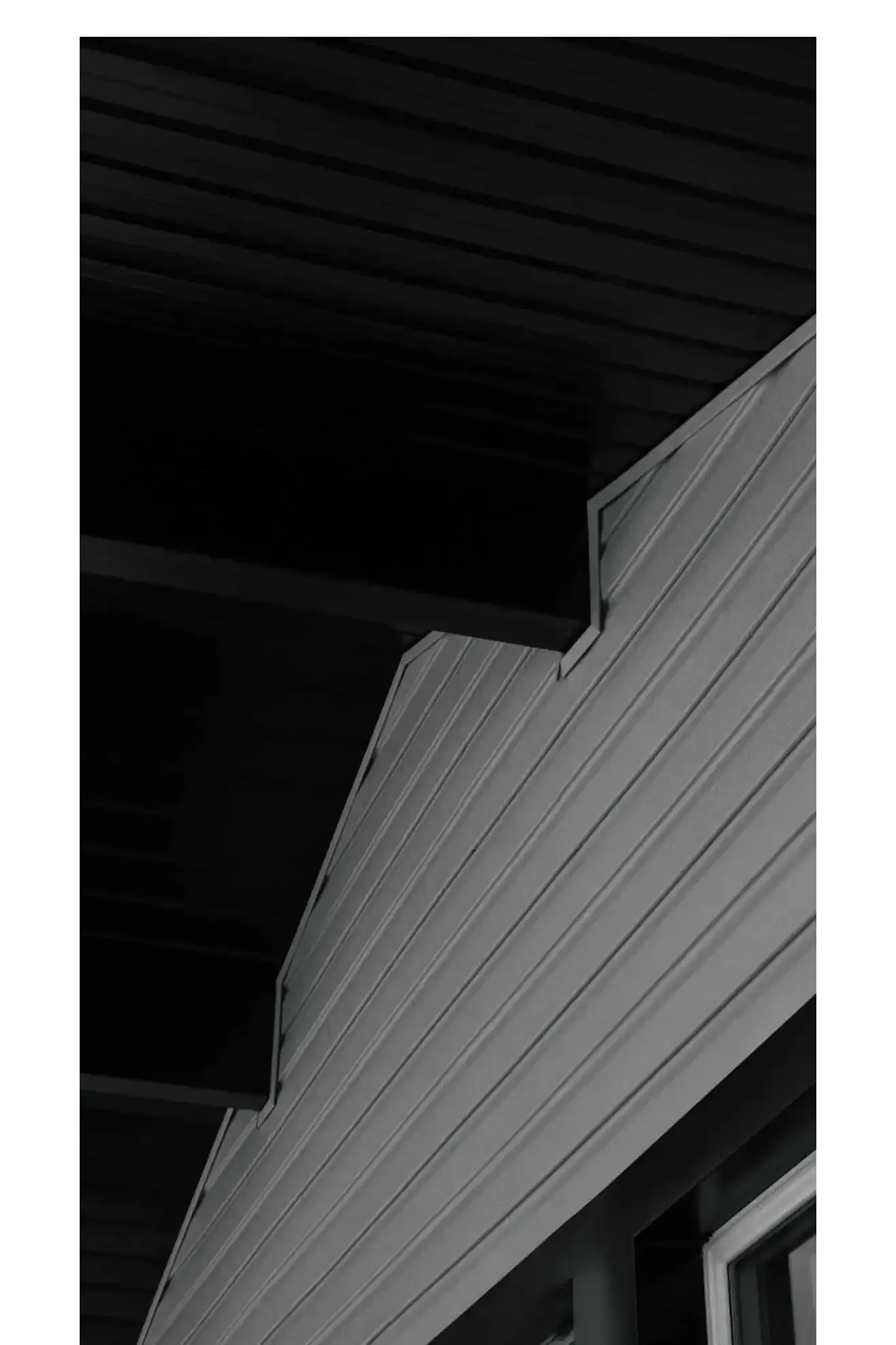 Exterior wall and roof of a building with horizontal siding in shades of gray.