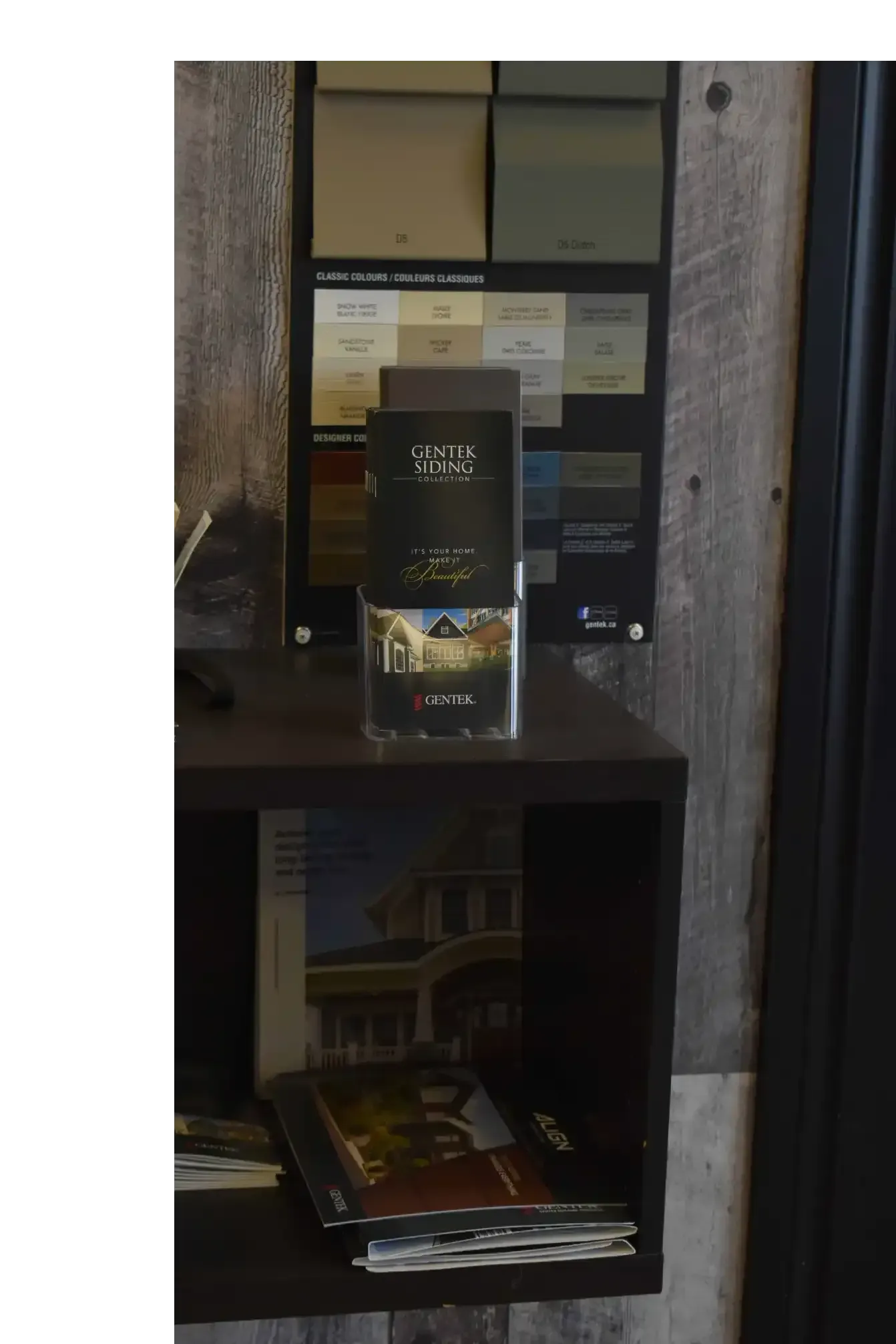 Shelf with paint color samples and brochures in front of a rustic wood wall.