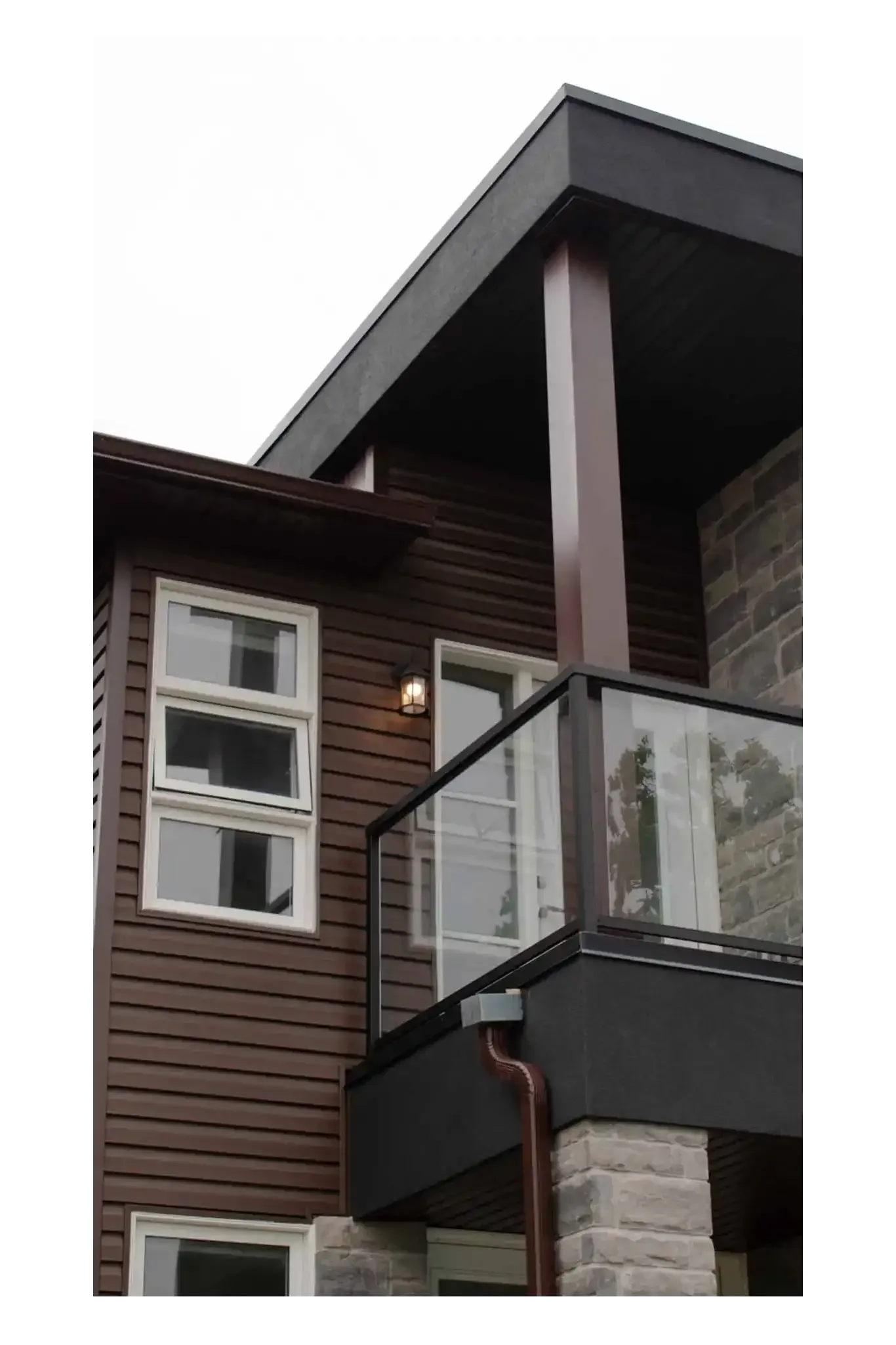 Brown and black house exterior with glass balcony and light-colored stone base.
