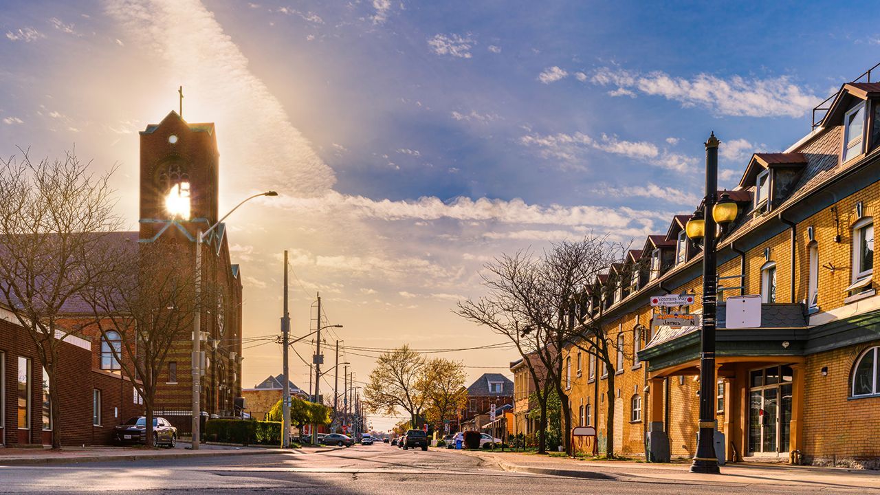 A city street with a church in the background and the sun shining through the clouds.