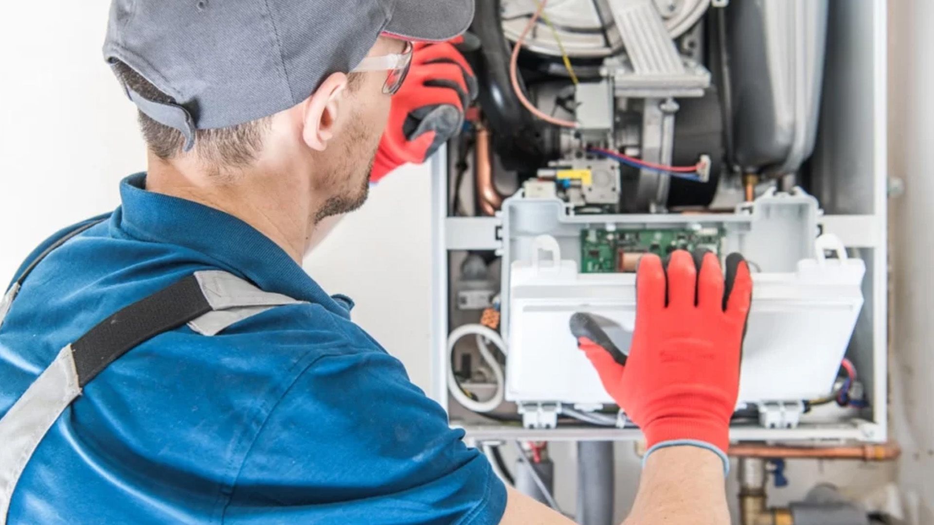 A man wearing red gloves is working on a boiler.