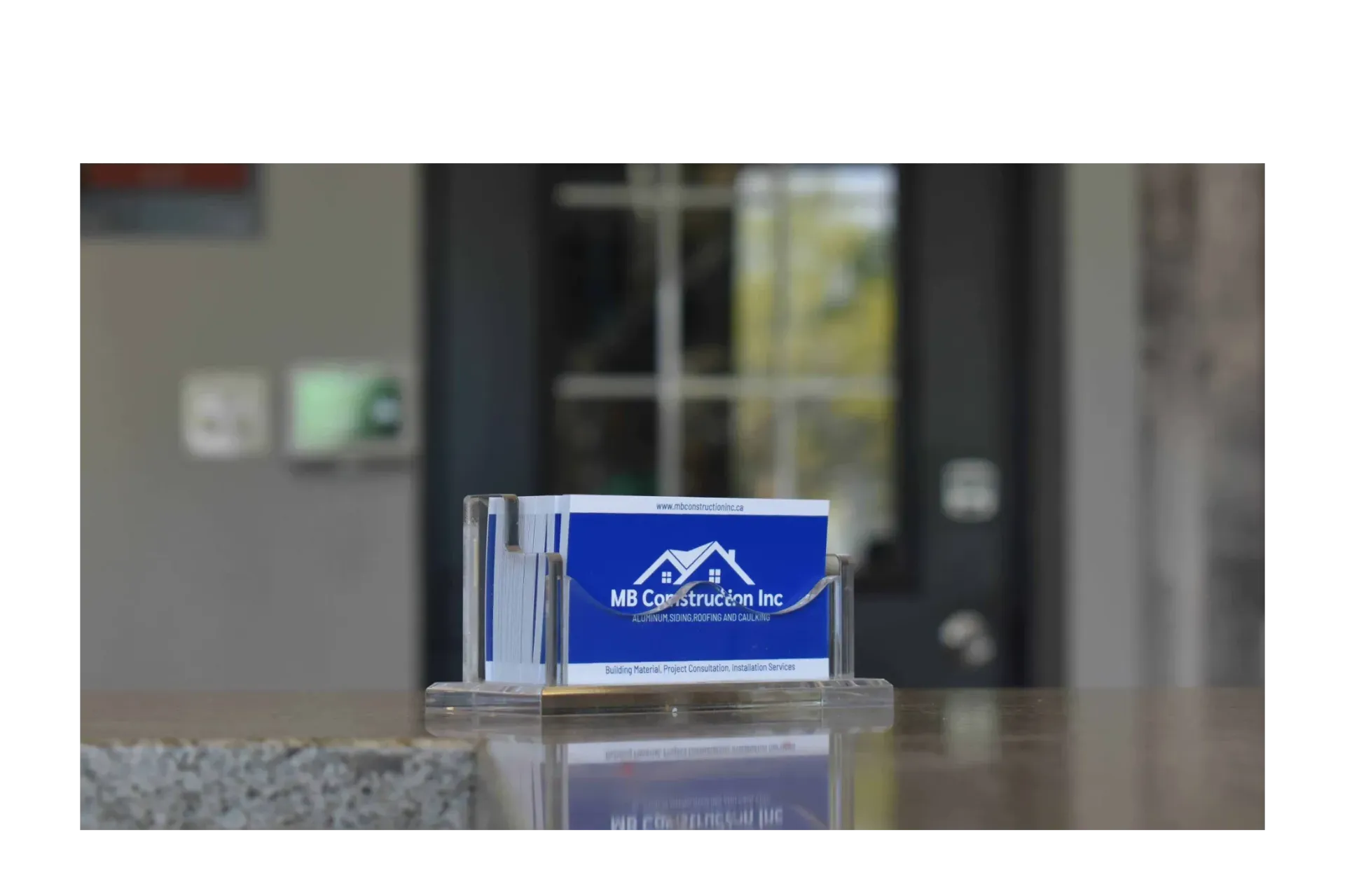 Business cards in a clear holder, blue card with white text, in front of a building.