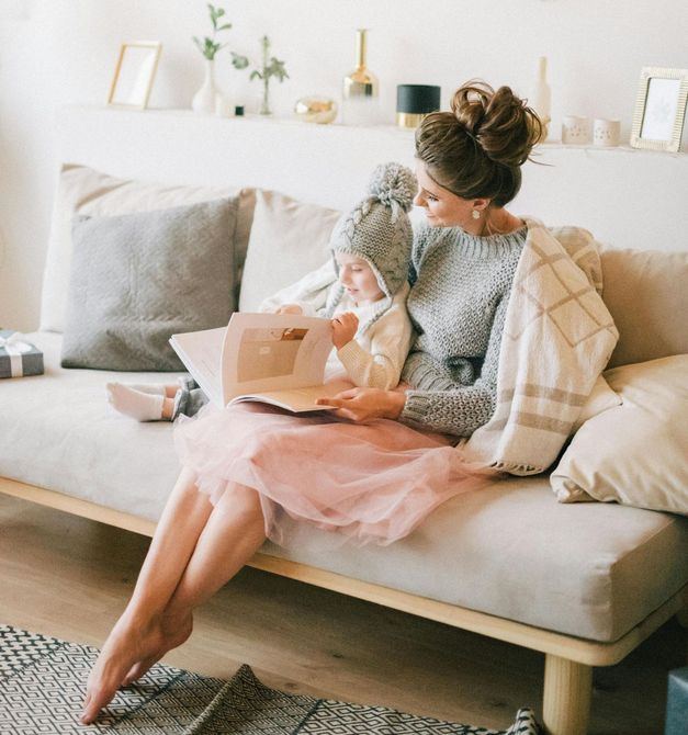 A woman is sitting on a couch holding a baby and reading a book