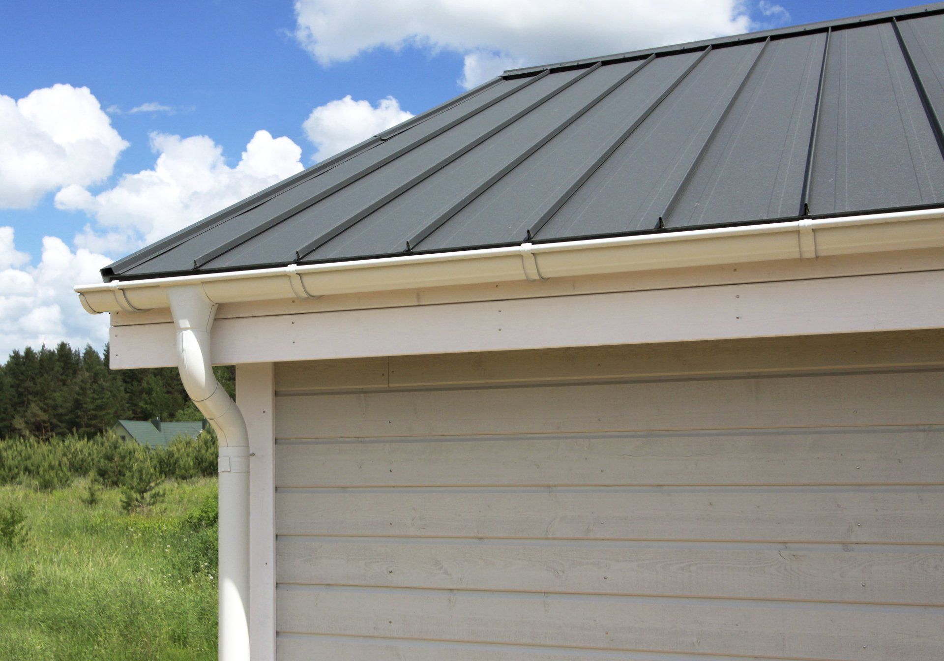 Gray metal roof and white gutter on a building against a blue sky with clouds