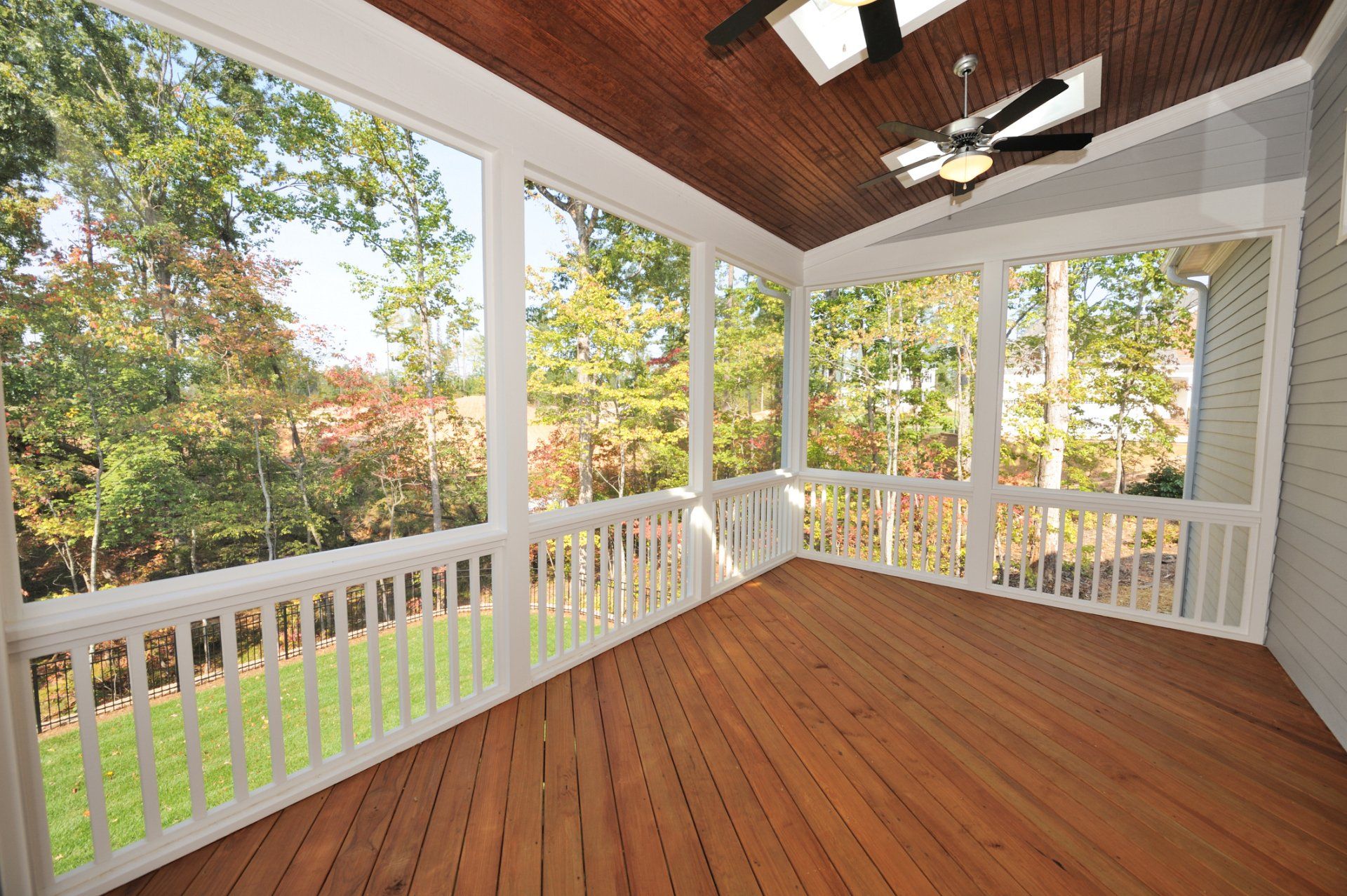 Covered wooden porch with white railings and screens overlooking a leafy yard