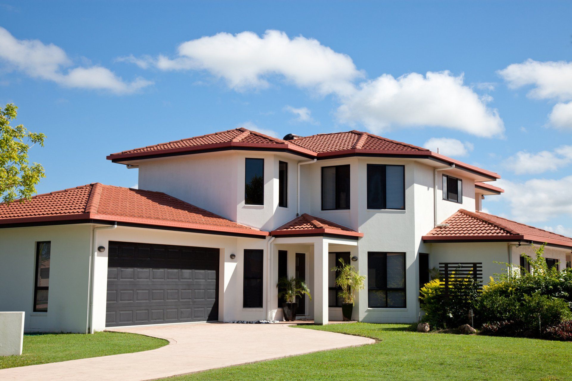 Modern two-story white house with red tile roof, garage, and green lawn under a blue sky