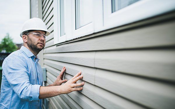 Man in hard hat examines siding on a house, outside.