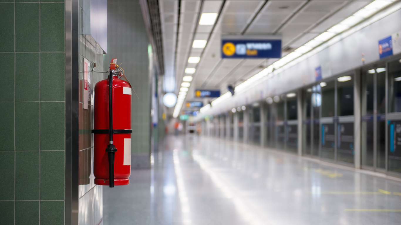 Red fire extinguisher mounted on a wall in a subway station hallway.