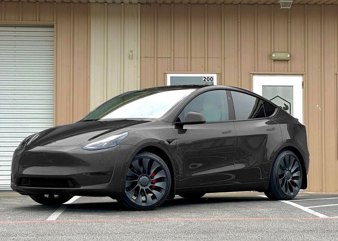 A black tesla model y is parked in front of a building.