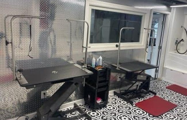 Interior of a pet grooming trailer with two grooming tables, supplies, and a window.