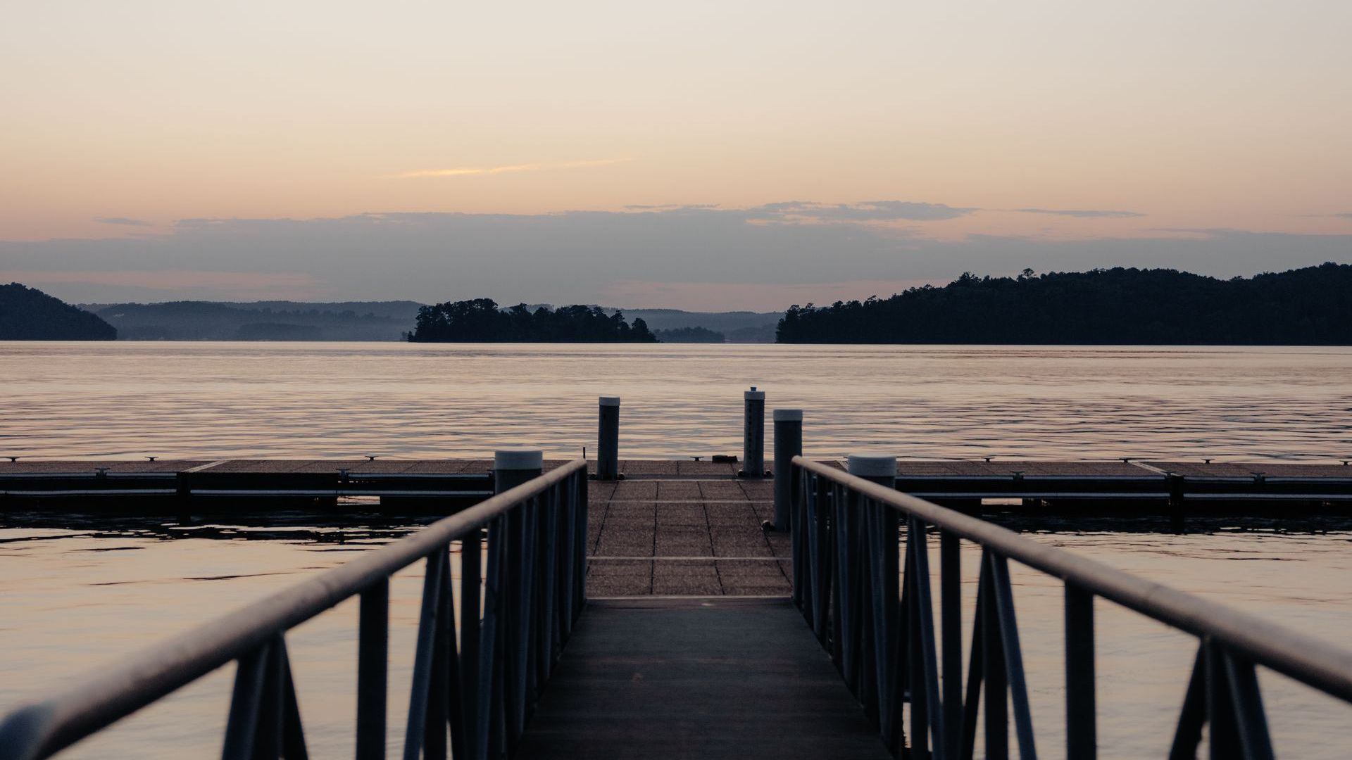 Dock extending over calm water at dusk, towards silhouetted islands.