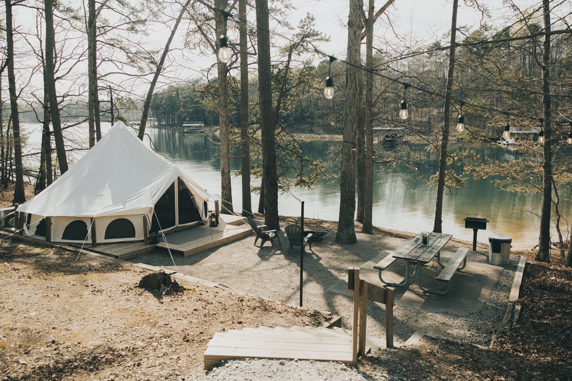 A canvas tent on a lakefront campsite with trees, picnic table, and string lights.