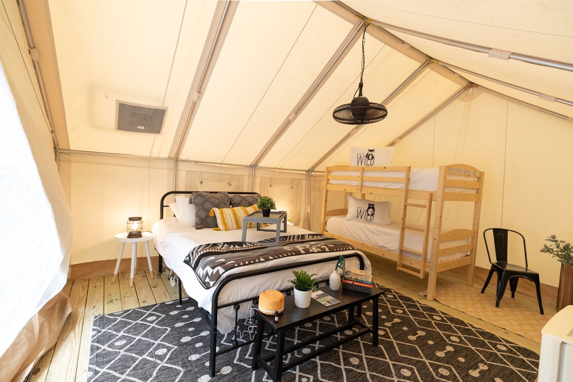 Interior of a glamping tent with a bed, bunk beds, rugs, and a hanging light.