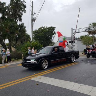 A black truck with a santa claus inflatable on the back is driving down a street.