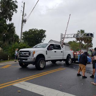 A white truck is driving down a street next to a group of people.