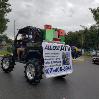A man is driving an atv with a sign on the back that says `` all out atv ''.