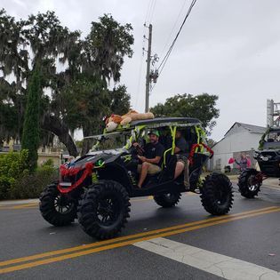 A man is riding a atv with a dog on top of it in a parade.