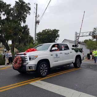 A white truck with a wreath on the front is driving down a street.