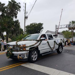A white truck decorated for christmas is driving down a street.