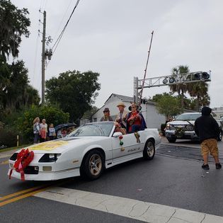 A group of people are riding in a white car in a parade.