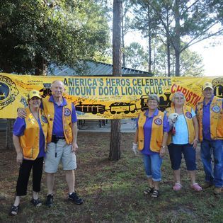 A group of people standing in front of a banner that says america 's heros celebrate mount dora lions club