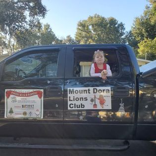 A little girl is sitting in the back of a truck that says mount dora lions club