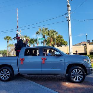 A gray truck with red bows on the doors is parked on the side of the road.