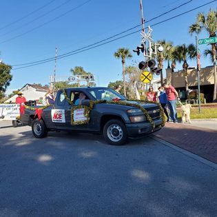 A truck decorated with flowers is driving down a street next to a train crossing.