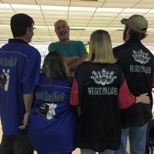 A group of people are standing in a bowling alley wearing shirts that say 