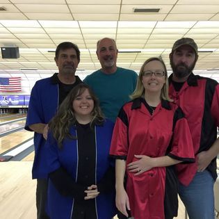 A group of people are posing for a picture in a bowling alley.