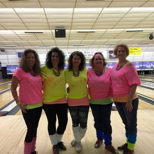 A group of women are posing for a picture in a bowling alley.