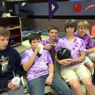 A group of boys wearing purple shirts are sitting in a bowling alley