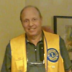 A man wearing a yellow vest with a lion on it is smiling for the camera.
