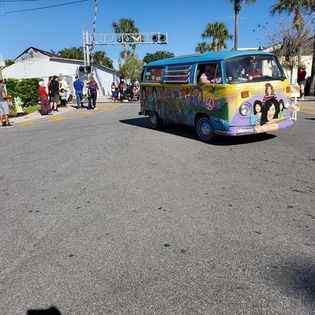 A hippie van is driving down a street in a parade.
