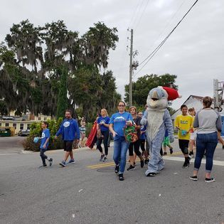 A group of people are walking down a street with a mascot in a dolphin costume.