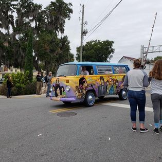 A group of people are standing in front of a hippie van.