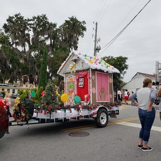 A gingerbread house on a trailer is being pulled down the street.