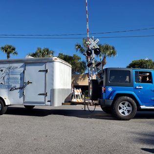 A blue jeep is towing a trailer down the road.