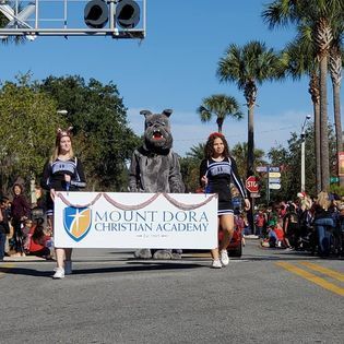A group of people are walking down a street holding a sign that says mount dora christian academy.