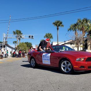 A red convertible mustang is driving down a street in a parade.