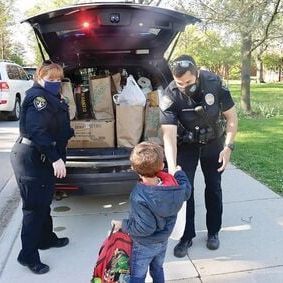 A police officer is helping a young boy with his backpack.